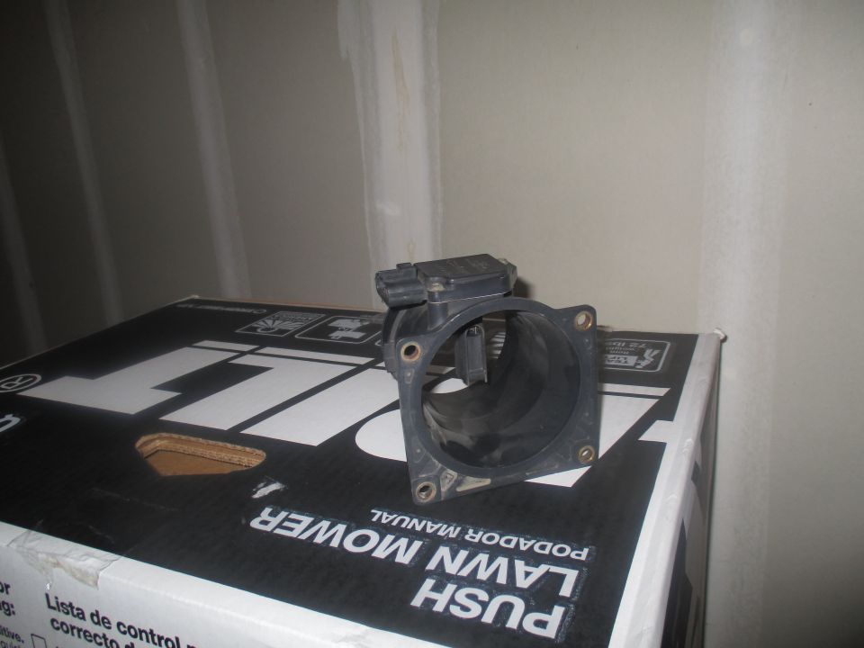 Black plastic mass air flow sensor with electrical connector, resting on a box
