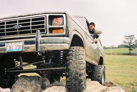 1986 Ford Bronco - A driver poses in a lifted Ford Bronco navigating a rocky trail.