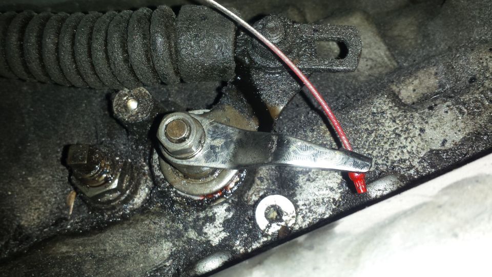 Close-up of a greasy automotive linkage with a red cap on a wire