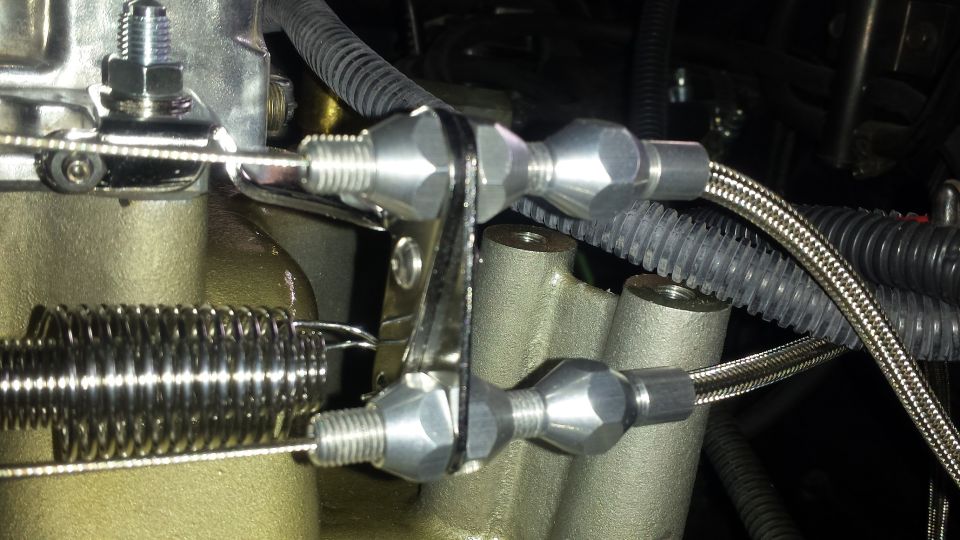 Close-up of throttle linkage connected to a carburetor with a large spring