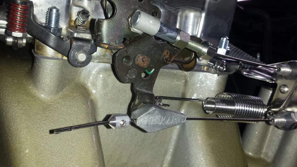 Close-up of a carburetor linkage with springs and cables. A part is labeled 'Holley'