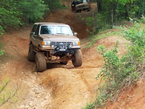 1988 Ford Bronco - This modified SUV navigates a challenging off-road trail, with another vehicle following closely behind.