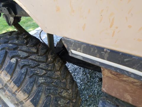1988 Ford Bronco - Close-up view of the side panel and tire of a tan SUV, showing off-road modifications.