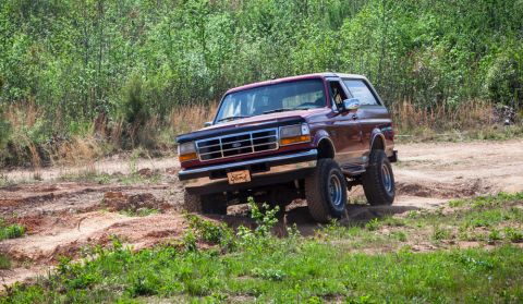 1995 Ford Bronco - A 1995 Ford Bronco navigates a rough, off-road path surrounded by greenery.