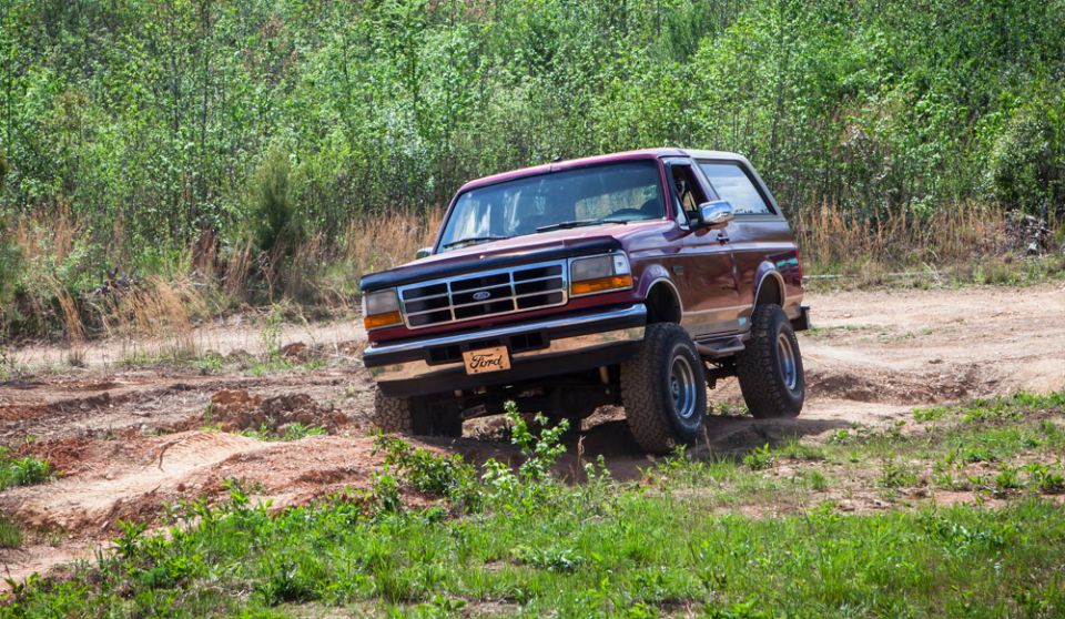 Maroon 1995 Ford Bronco driving on a dirt trail with trees in the background