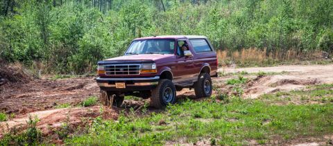 1995 Ford Bronco - A maroon 1995 Ford Bronco navigates a muddy, wooded trail.