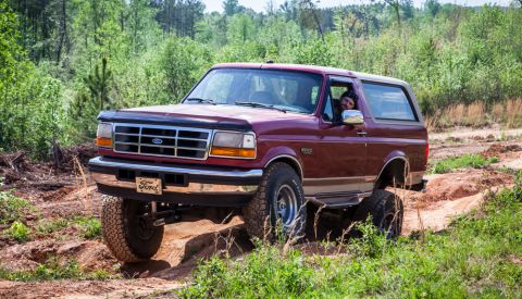 1995 Ford Bronco - A maroon Ford Bronco navigates an off-road trail with a driver visible.