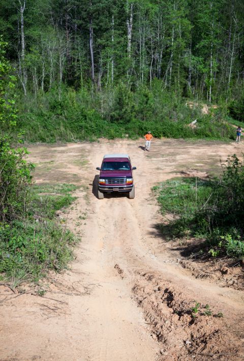 1995 Ford Bronco - A maroon Ford Bronco navigates a dirt path through a wooded area.