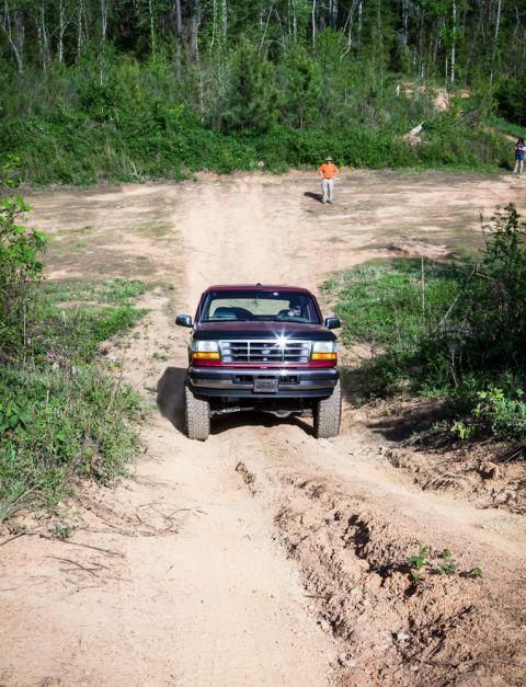 1995 Ford Bronco - A red 1995 Ford Bronco navigates a dirt path through a wooded area.