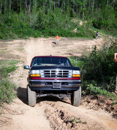 1995 Ford Bronco - A 1995 Ford Bronco navigates a challenging dirt path surrounded by lush green foliage.