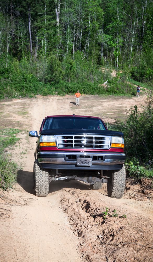 Red and black Ford truck with lifted suspension driving on a dirt road