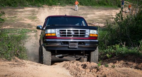 1995 Ford Bronco - A red and black Ford Bronco navigates an off-road trail with a lifted suspension and large tires.