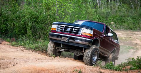 1995 Ford Bronco - This Ford Bronco is navigating an off-road trail, kicking up dust as it climbs.