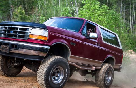 1995 Ford Bronco - This lifted Ford Bronco navigates a dusty trail, its driver visible behind the wheel.