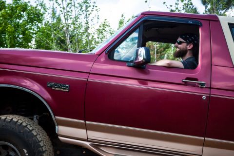 1995 Ford Bronco - Driver of a red 1995 Ford Bronco with tan trim, seen from the side.