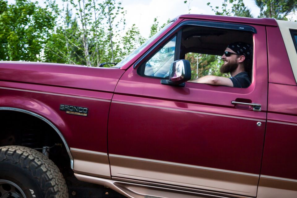 Red 1995 Ford Bronco with tan trim, driver wearing sunglasses and bandana