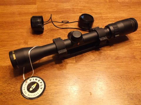 1995 Mercury Grand Marquis - Bushnell Elite rifle scope with lens caps and a "Firefly Reticle" tag on a wooden surface.