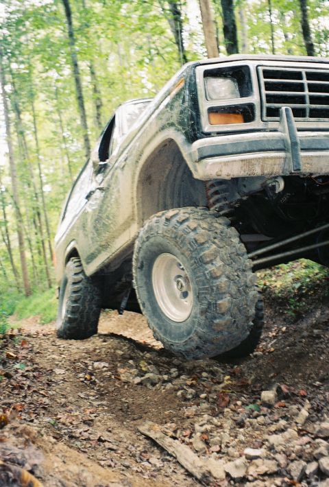 1986 Ford Bronco - This lifted Ford Bronco navigates a challenging off-road path through a forest.