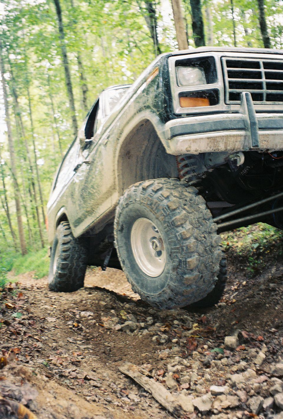 Ford Bronco climbing a dirt trail in a wooded area. Front wheel is angled up