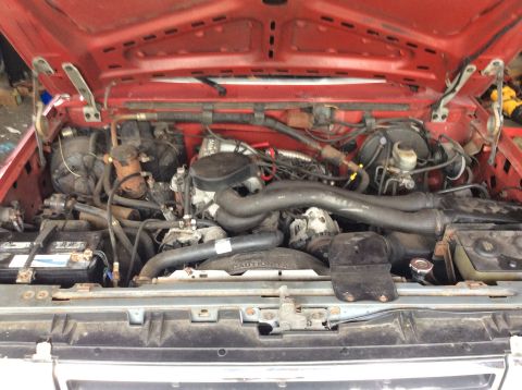 1989 Ford Bronco - The engine compartment of a vehicle is shown with the hood open, revealing various mechanical parts.