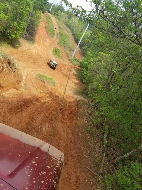 1988 Ford Bronco - Off-road vehicles navigate a steep, muddy trail surrounded by lush green trees.