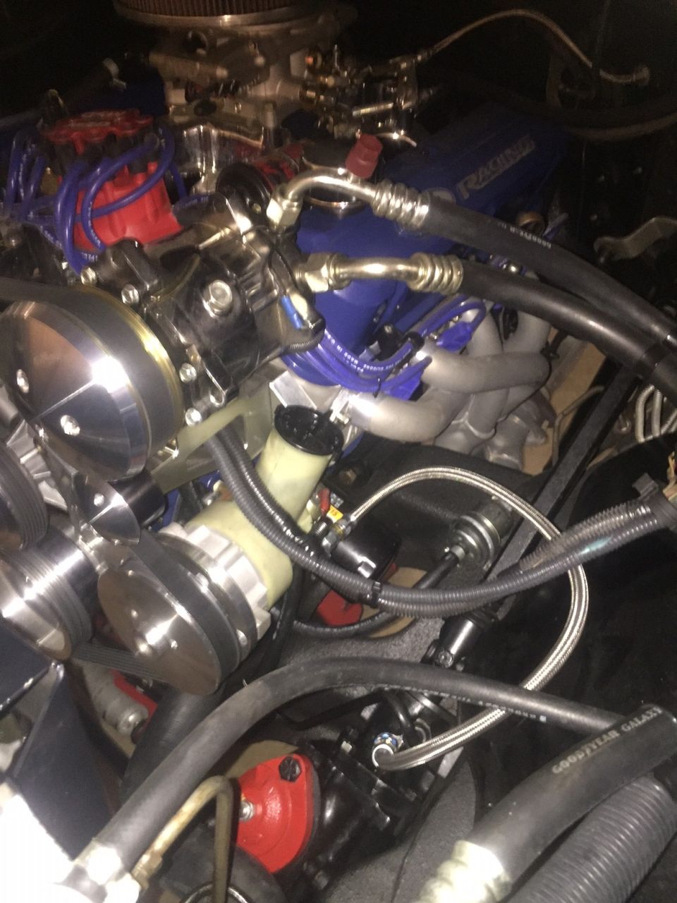 Engine bay with V8 engine, blue valve covers, and chrome components. Includes power steering reservoir and brake lines