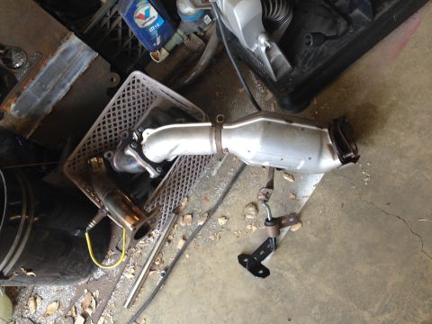 2015 Subaru Impreza - A removed catalytic converter sits on the floor, showing its metallic casing and exhaust pipe connections.