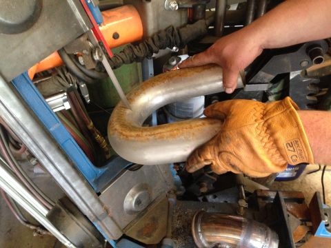 2015 Subaru Impreza - A gloved hand guides a bent exhaust pipe during a repair or fabrication process.