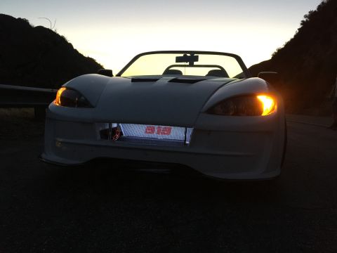 2015 Subaru Impreza - Front view of a white convertible sports car with its turn signal on and an illuminated grille displaying '913'.