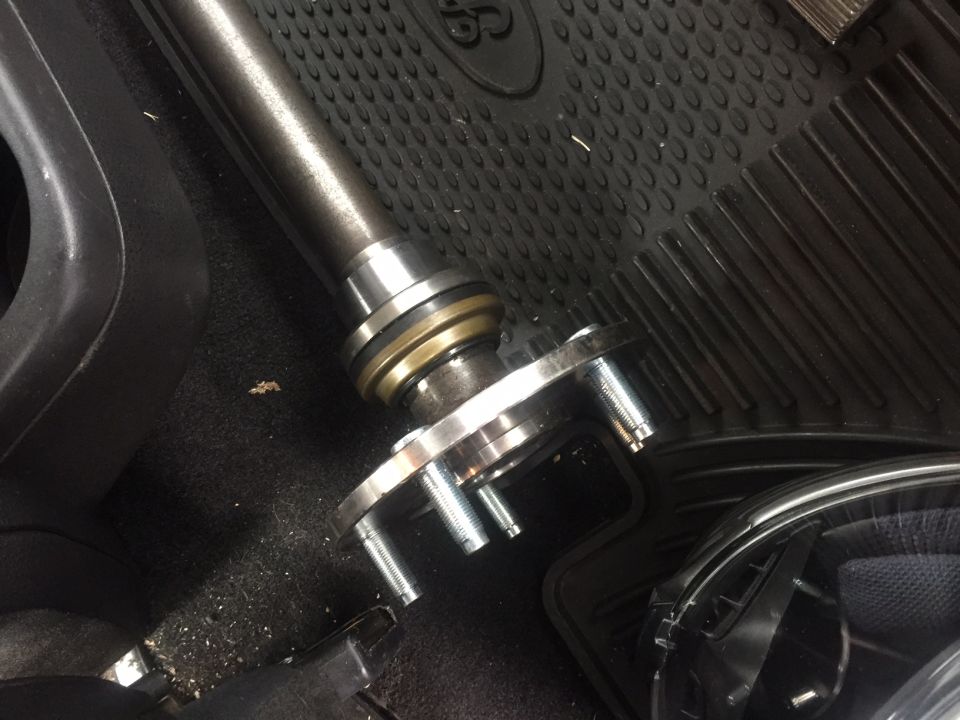 Axle shaft and hub assembly with four studs on a black floor mat inside a vehicle