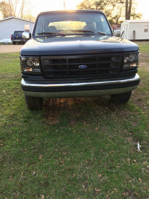 1996 Ford Bronco - The front of a dark-colored Ford Bronco is shown, with a suburban house and another vehicle in the background.