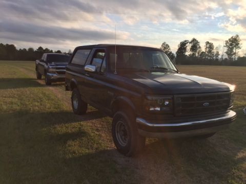 1996 Ford Bronco - A 1996 Ford Bronco and another truck sit in a field under a cloudy sky.