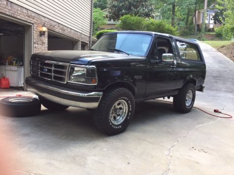 1996 Ford Bronco - A black Ford Bronco is parked in a driveway with a spare tire nearby.