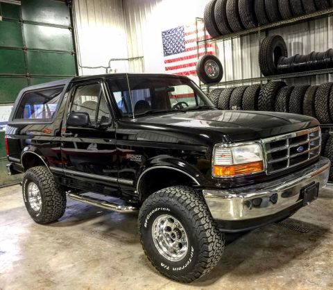 1996 Ford Bronco - A black 1996 Ford Bronco is shown from a three-quarter front angle in a garage with tires stacked in the background.