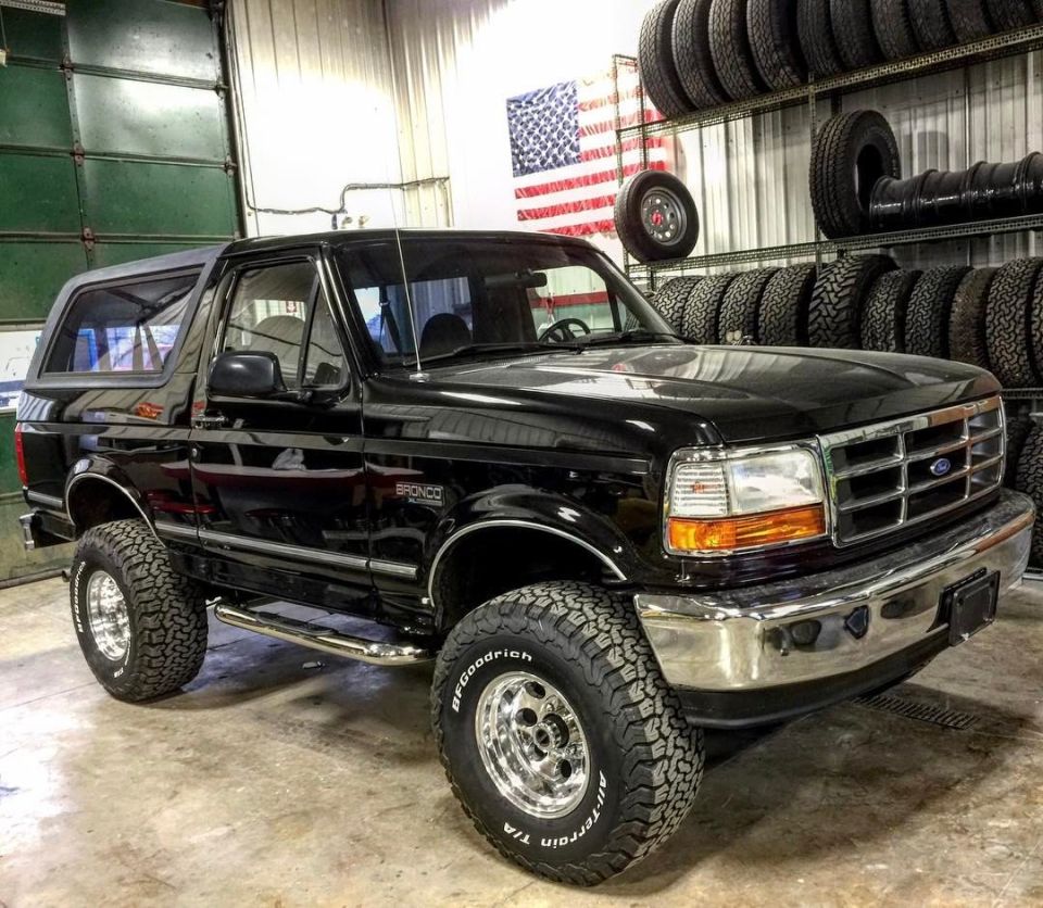 Black 1996 Ford Bronco with chrome wheels and side steps parked indoors