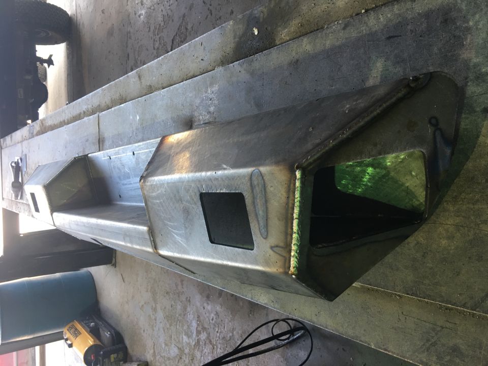 Custom steel bumper with angular cutouts and visible welds, resting on a workbench.