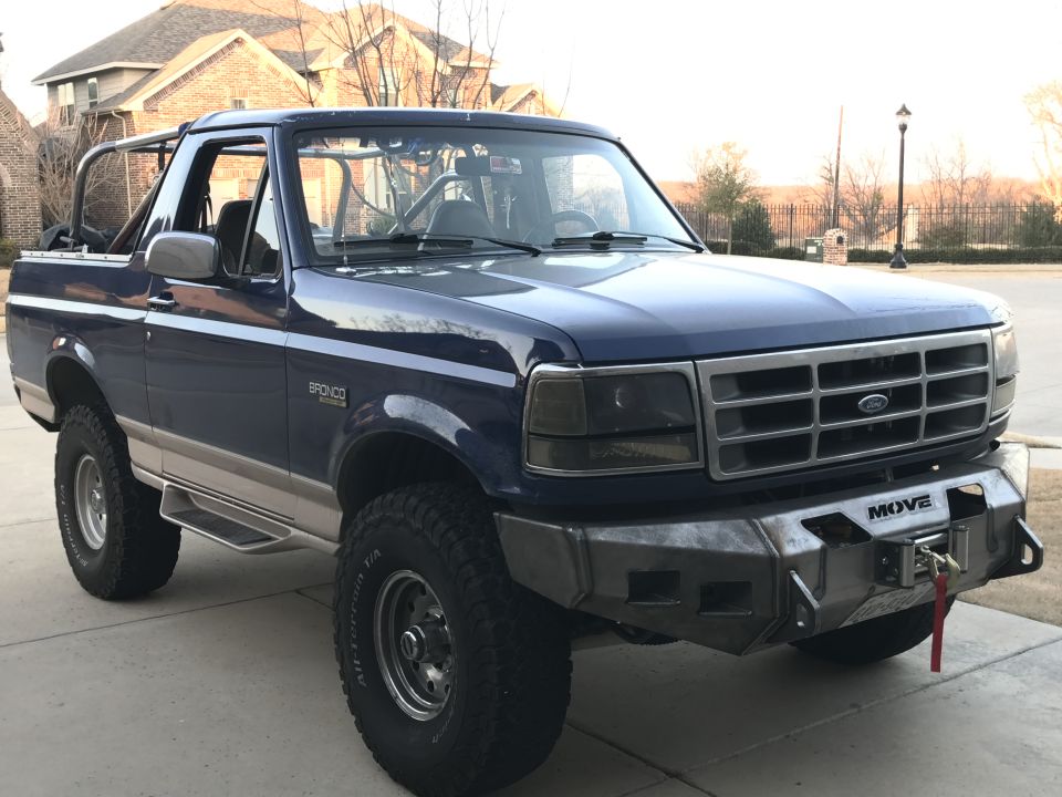 Blue 1996 Ford Bronco with custom bumper and winch, off-road tires, and roll cage.