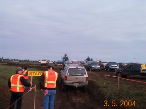 1983 Ford Bronco - Vehicles gathered at the start line of an off-road event on a cloudy day.