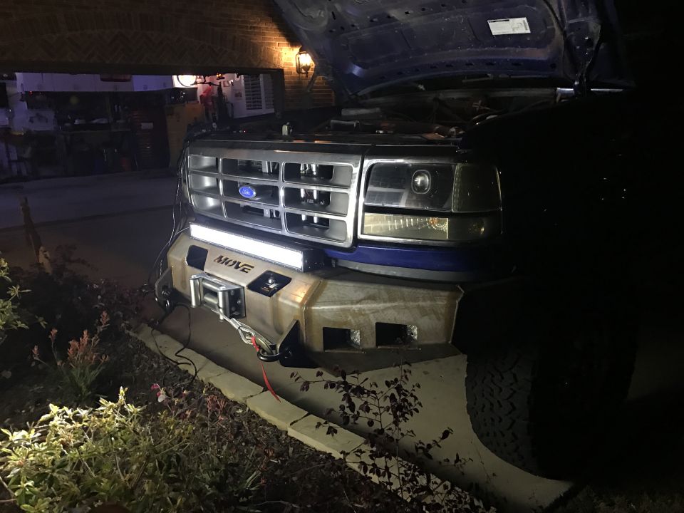 Blue Ford truck/SUV front end with aftermarket bumper, winch, and light bar. Hood is open.
