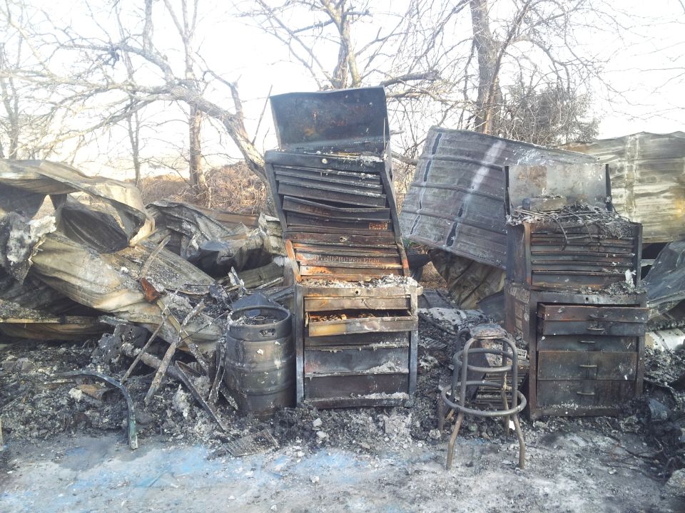 Charred debris from a fire including tool chests, a barrel, and a stool.