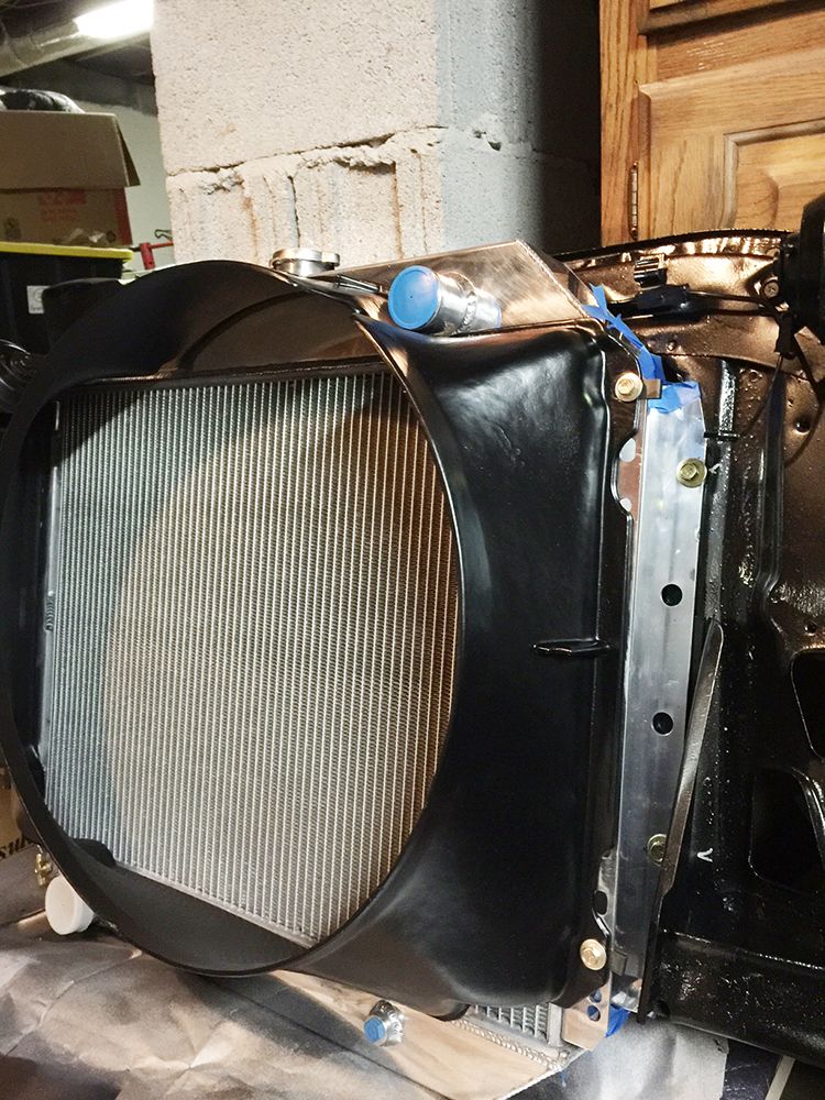 Vehicle radiator assembly with black shroud and aluminum fins, showing mounting hardware.