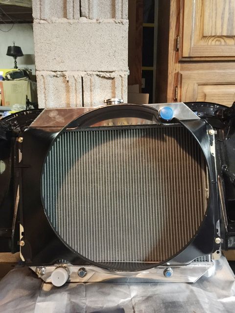 1978 Ford Bronco - A new aluminum radiator is installed in the front of a classic vehicle, likely a Ford Bronco, with a black shroud and chrome cap.