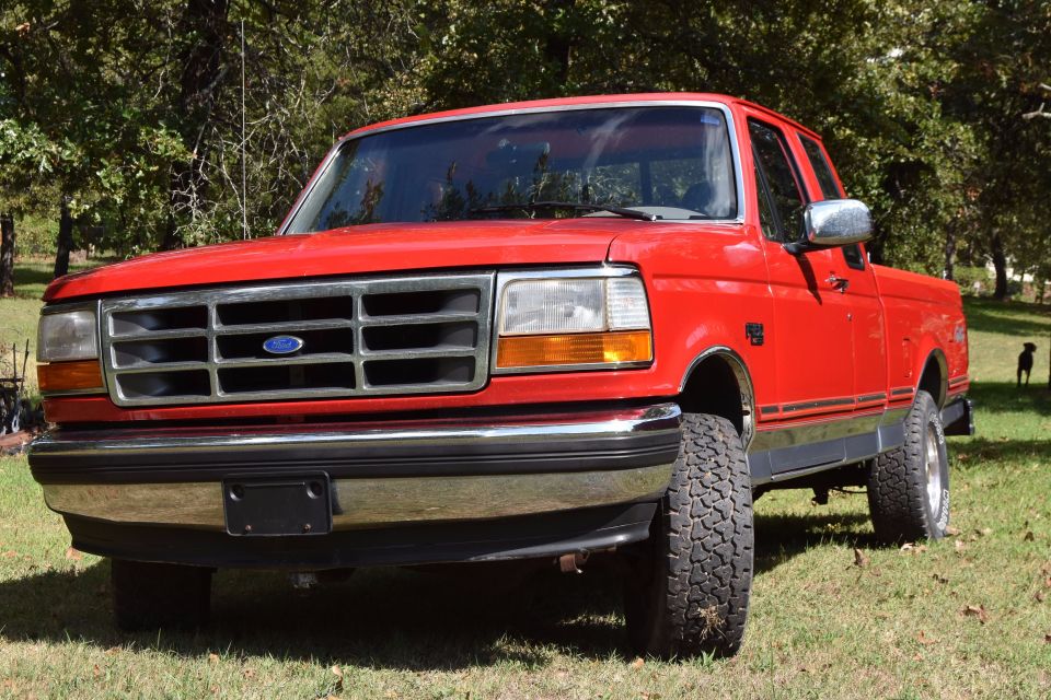 Red Ford extended-cab 4x4 pickup on grass, low front three-quarter view with chrome grille and all-terrain tires