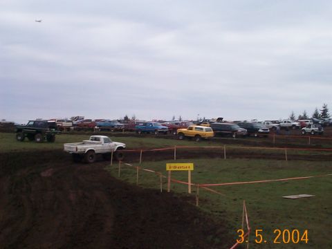 1983 Ford Bronco - A muddy off-road event with numerous trucks and SUVs gathered under an overcast sky.