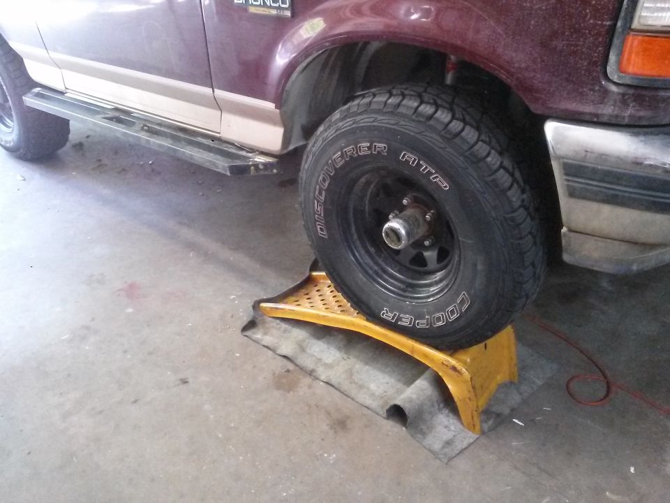 Maroon Ford Bronco front passenger wheel on a yellow ramp, showing side steps.