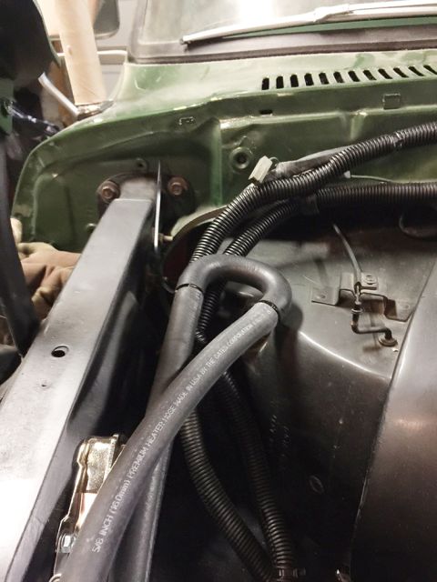 1978 Ford Bronco - A close-up view of the engine bay of a green 1978 Ford Bronco, focusing on the heater hoses and wiring harnesses. Text on one of the hoses…