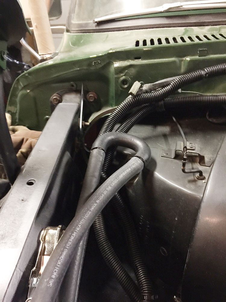 Engine bay of a green 1978 Ford Bronco showing heater hoses and wiring.