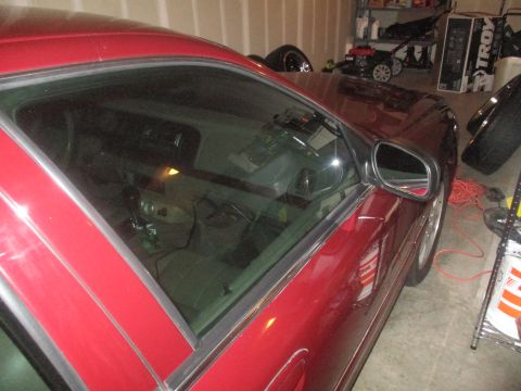 2004 Ford Crown Victoria - The driver's side of a red sedan is shown parked in a garage. The vehicle's interior is visible through the tinted windows, and a side mirr…