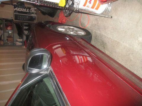 2004 Ford Crown Victoria - A red sedan is parked in a garage, with a side mirror and part of the front fender visible. The vehicle is angled, showing the side of the…