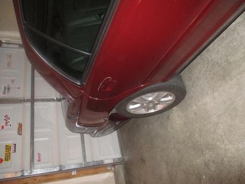 2004 Ford Crown Victoria - The rear passenger side of a dark red sedan is shown parked in a garage. The vehicle has tinted windows and a silver alloy wheel is visible.